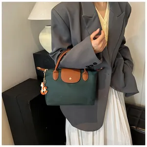 Detail of dark green nylon tote bag featuring brown leather handles and a horse charm