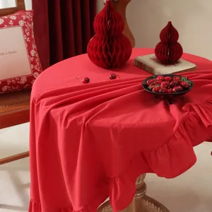 Detailed view of red round cotton tablecloth with elegant ruffled edges on a wooden table