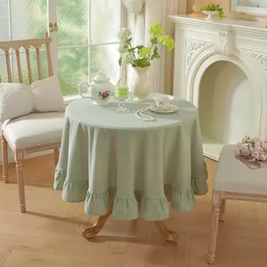 Detailed view of sage green round tablecloth with ruffled edges in a French rural setting