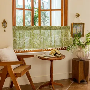 Detailed view of green cafe curtain with white leaf patterns and fringe tassels