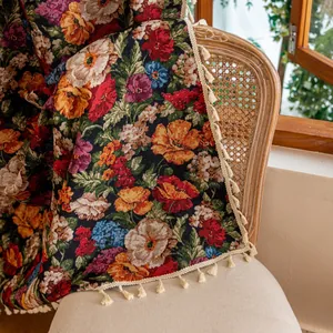 Vintage bloemengeweven wandkleed met witte kwastjes gedrapeerd op een rotan stoel