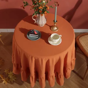 Detail of orange round cotton linen tablecloth featuring decorative ruffled edges and texture