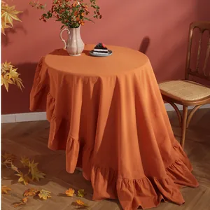 Detail of warm orange round cotton tablecloth with ruffle edge on a wooden table