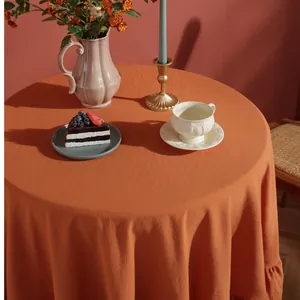 Detail of round orange linen tablecloth with ruffled edges in a warm tea setting