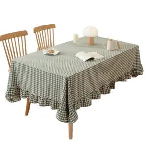 Green and white gingham cotton tablecloth with ruffled edges on a rustic wooden dining table