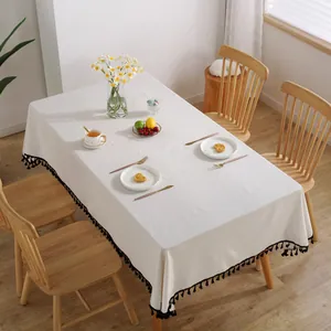 Detail der weißen Baumwoll-Leinen-Tischdecke mit schwarzen Bommelfransen auf Holztisch
