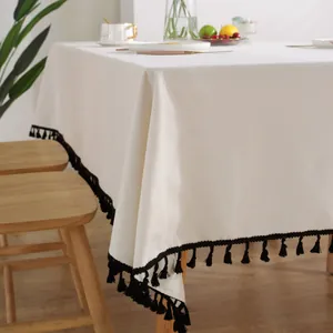 Detailansicht der cremeweißen Baumwoll-Leinen-Tischdecke mit schwarzen Quasten am Rand