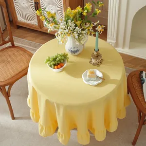 Detailed view of cream ruffled round tablecloth with elegant drape on wooden table