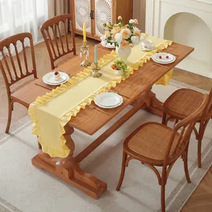 Detail van een lichtgele tafelloper met elegante ruches op een donkere houten tafel