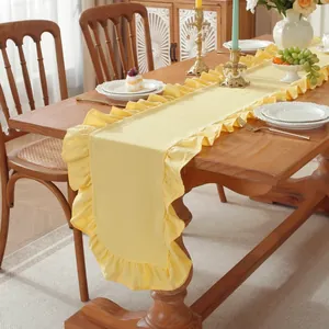 Detail van een gele katoenen tafelloper met ruches aan de randen op een houten tafel