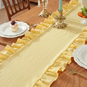 Detail van de lichtgele tafelloper met geplooide ruches op een houten eettafel