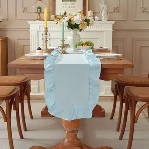 Detail van lichtblauwe katoenen tafelloper met romantische ruches op een houten tafel