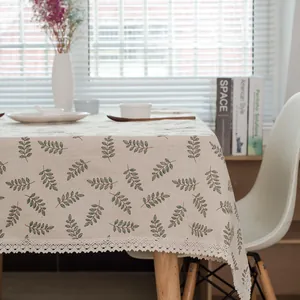 Détail de la nappe en lin avec des motifs de feuilles vertes et une bordure en dentelle