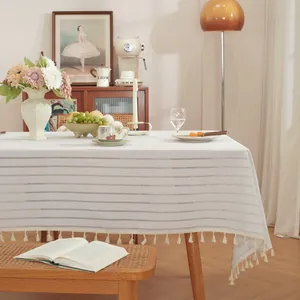 Detail van beige gestreept linnen tafelkleed met decoratieve kwastjes op houten tafel