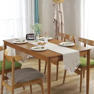 Detail of striped linen table runner with decorative pom-pom fringe on a wooden table