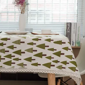 Détail de nappe en lin avec motifs de pins verts et bordures en dentelle creuse