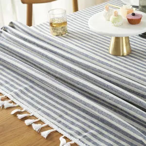 Detail van blauw-wit gestreept tafelkleed met witte franjes en kwastjes op houten tafel