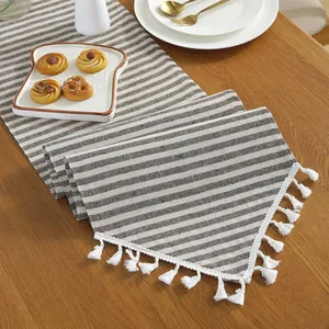 Brown and cream striped cotton linen table runner with white fringe on wooden table