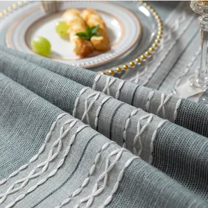Dettaglio della tovaglia in lino grigio-blu con ricamo bianco a X e strisce sottili