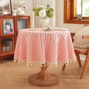 Detail of pink striped cotton linen tablecloth featuring decorative cream fringe tassels
