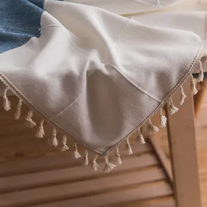 Dettaglio di tovaglia in lino blu e beige con trama rustica e bordi sfrangiati con nappe
