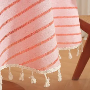 Detail of orange striped round tablecloth with elegant beige tassel fringe on wood