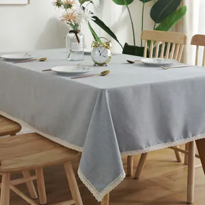 Grijs rechthoekig tafelkleed met witte kantranden op een houten tafel in huis
