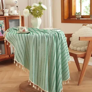 Close-up of green and white striped cotton linen tablecloth with cream tassel fringes