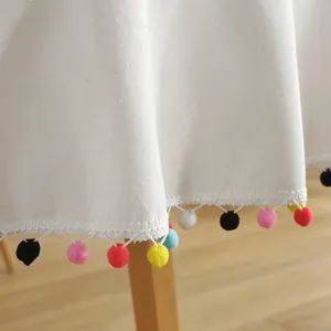 White canvas tablecloth with colorful pom-pom fringe and festive holiday decorations