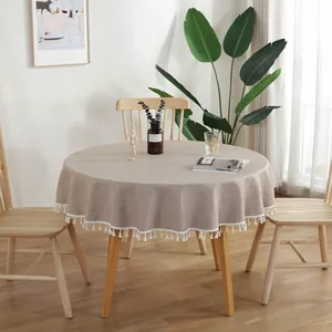 Detailopname van een beige rond tafelkleed met elegante witte franjes op houten tafel