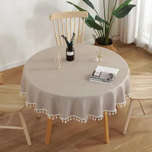 Detail van rond beige linnen tafelkleed met decoratieve witte pomponrand voor binnen