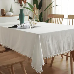 Detail of solid white rectangular tablecloth featuring delicate pom-pom fringe and cotton texture