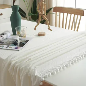 Detail of white cotton table runner with decorative pom-pom fringe and woven texture