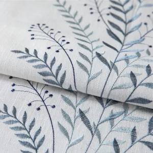 Ricamo dettagliato di foglie blu su tovaglia in lino grigio strutturato con nappe