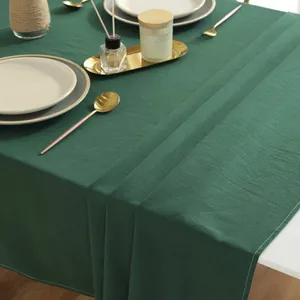 Close-up of deep green cotton tablecloth with fine white stitching and linen texture