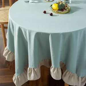 Detail of mint blue cotton linen tablecloth with beige ruffled edges on a round table