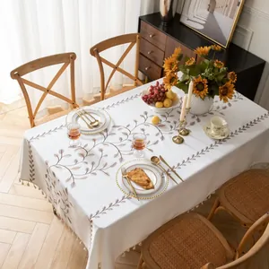 Dettaglio della tovaglia in lino beige con motivi a foglie e bordi decorativi a frange