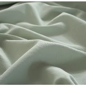 Macro detail of soft light green washed cotton fabric showing natural wrinkled texture