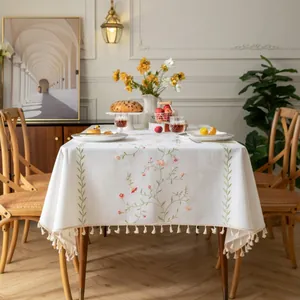 Dettaglio di fiori rosa ricamati e nappe beige su una tovaglia in cotone e lino