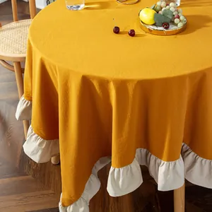 Detailed view of ginger yellow round tablecloth with elegant cream ruffled edges