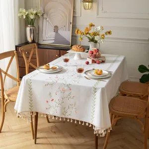 Dettaglio del ricamo floreale rosa e nappine beige su una tovaglia di cotone e lino grigio
