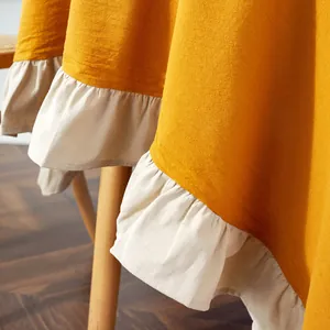 Detail of mustard yellow textured tablecloth featuring cream white ruffled edges and drapes