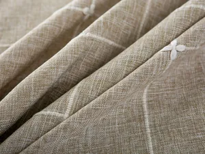 Macro view of beige faux linen tablecloth with white plaid lines and floral embroidery