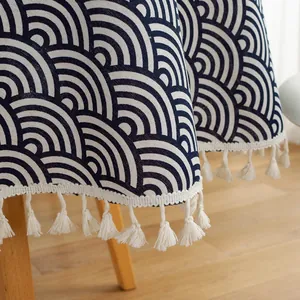 Detail of blue wave pattern tablecloth with white fringe tassels on a wooden surface