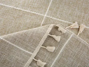 Macro shot of embroidered beige checkered tablecloth featuring fine white tassels and texture
