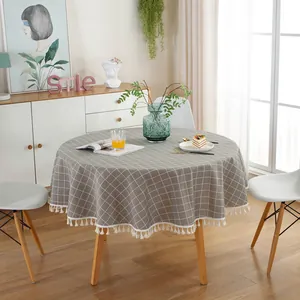 Detail of grey checkered round tablecloth with white tassel edge on wooden table