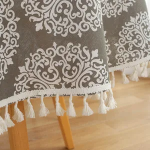 Detail of round grey tablecloth with white floral pattern and cream cotton tassels