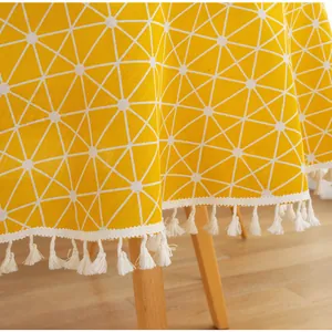 Macro detail of yellow geometric tablecloth featuring white tassels on wooden table