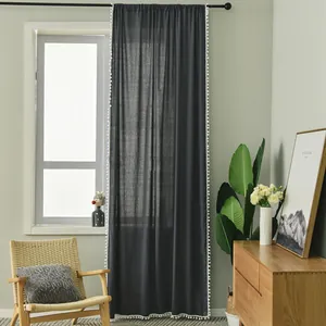 Detail of dark grey sheer curtain with white pom-pom fringe edge in a cozy room