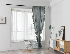 Detail of greyish-blue ruffled edge curtains hanging with white sheer lace drapes